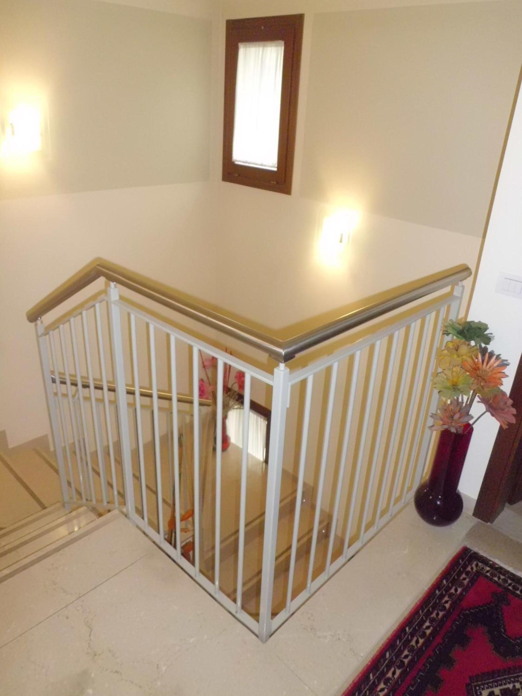 A staircase with a white railing and a vase with flowers on the landing.