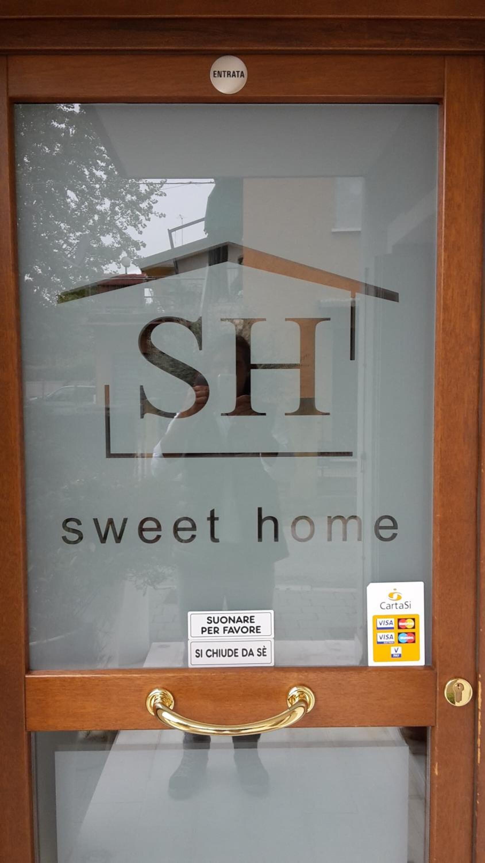 Una puerta de cristal con un letrero que dice "SH sweet home" y una etiqueta que dice "SUONARE PER FAVORE".