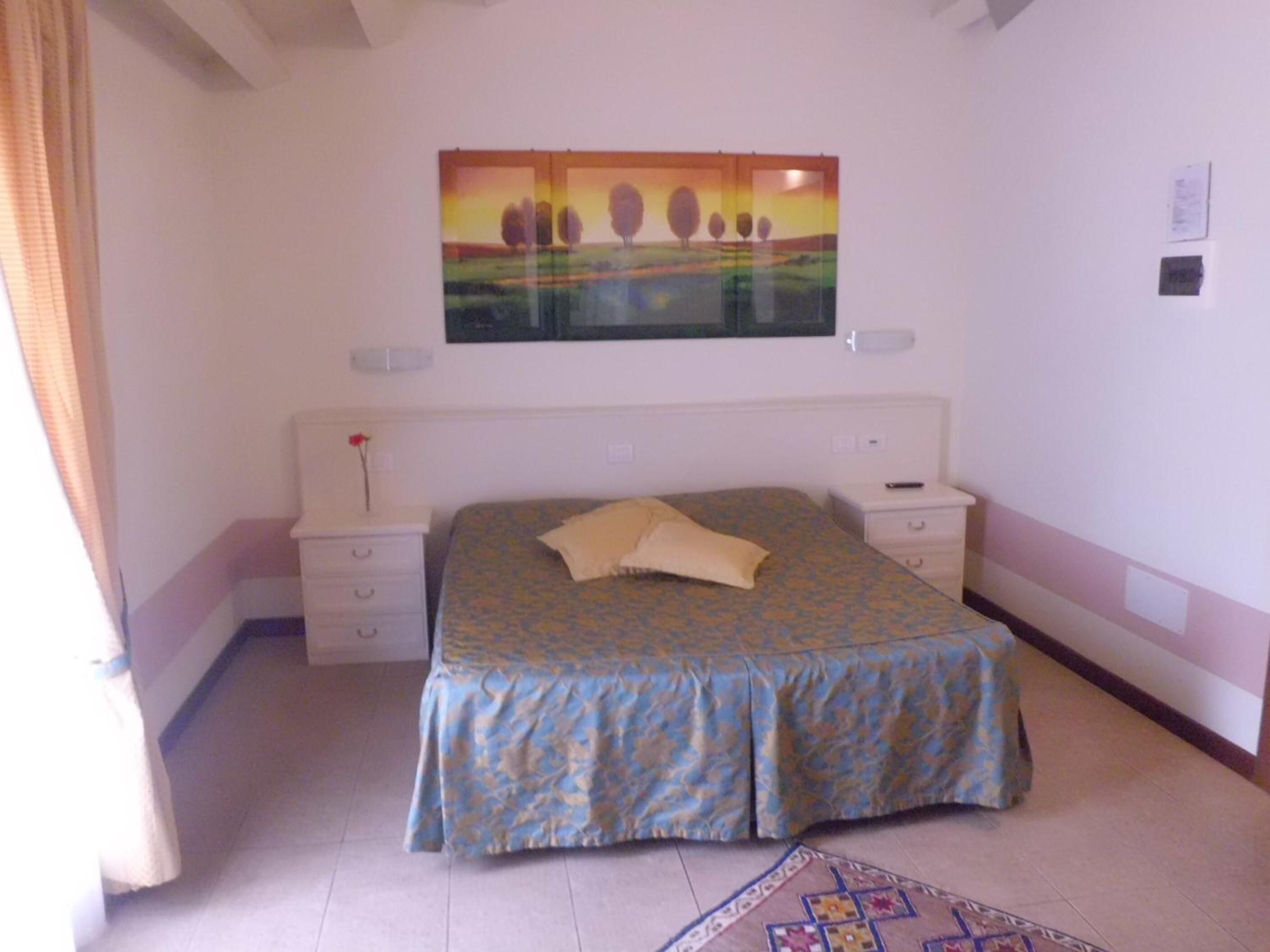 Ein Schlafzimmer mit Bett, Nachttischen, einem Gemälde und einem Fenster mit Vorhängen.