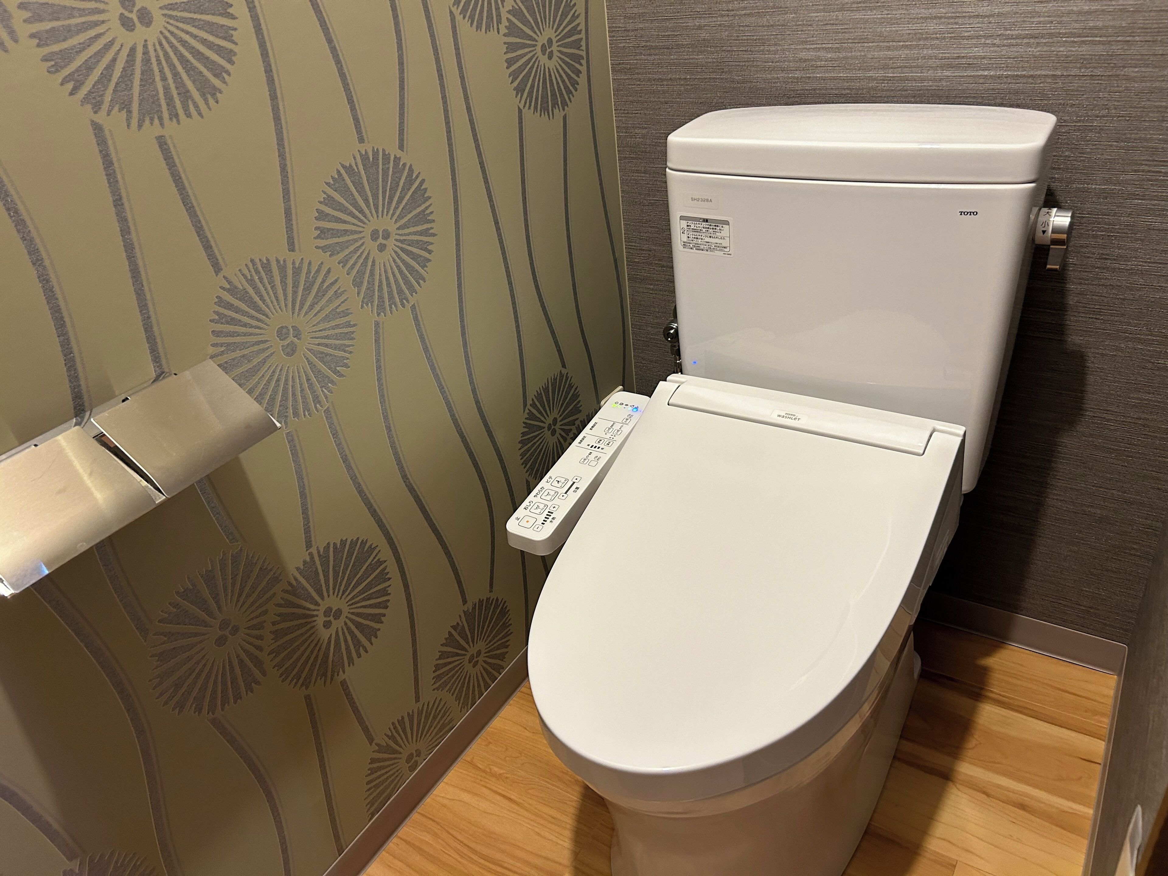 A toilet with a control panel, a toilet paper holder, and a wall with a floral pattern.