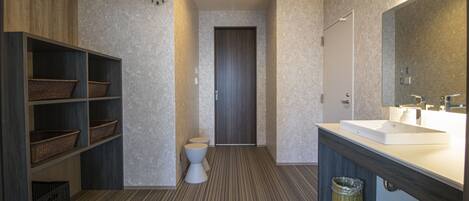 Un baño moderno con un espejo grande, un lavamanos y un inodoro. Hay repisas con cestas y un bote de basura.