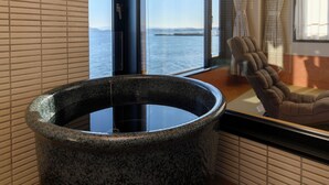 Et spaområde med et stenhottub, et vindue med havudsigt og en stol.