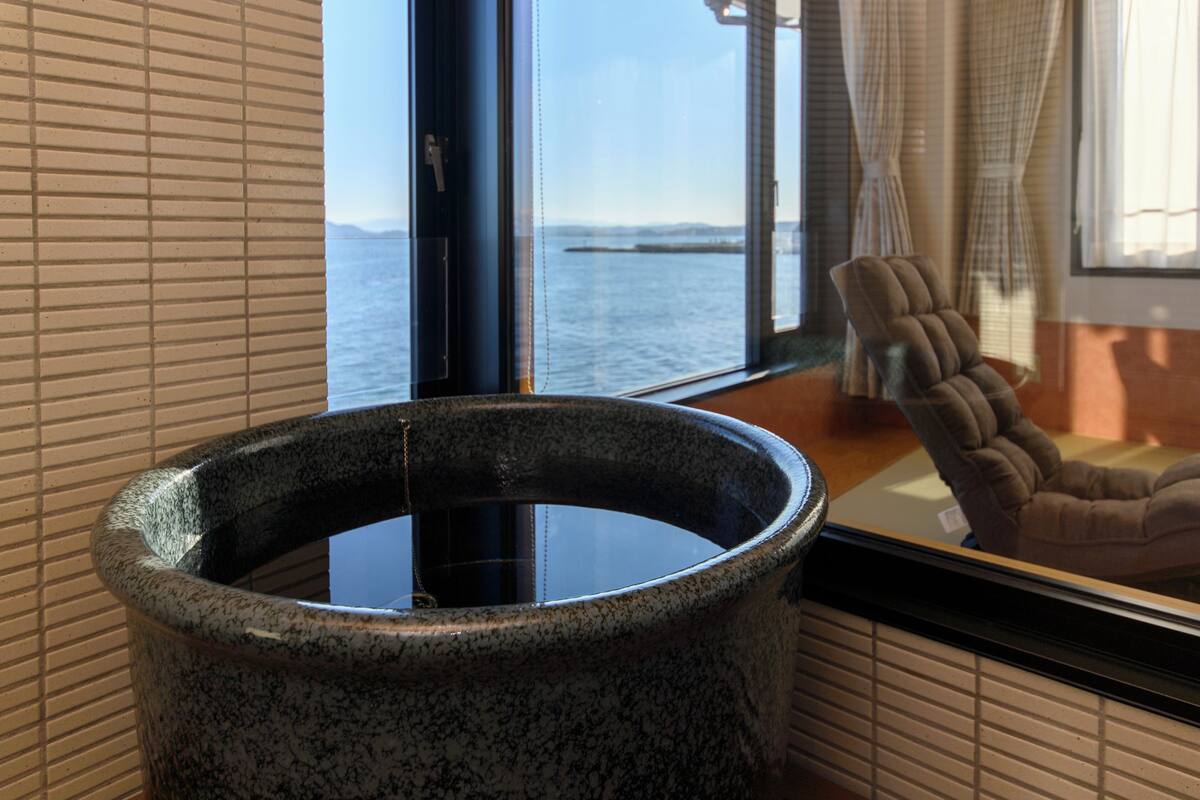 Un área de spa con un jacuzzi de piedra, una ventana con vistas al mar y una silla.