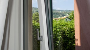 Vista a través de una ventana con una puerta, mostrando una colina con vegetación y edificios al fondo.