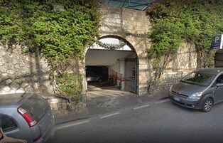 A stone archway leading to a building with a parking area.