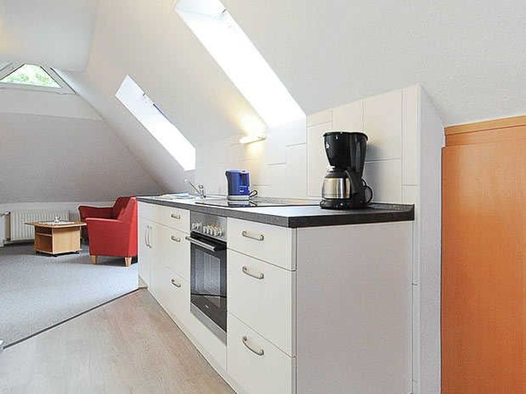 A compact kitchen with a built-in oven, a coffee maker, and a red chair.