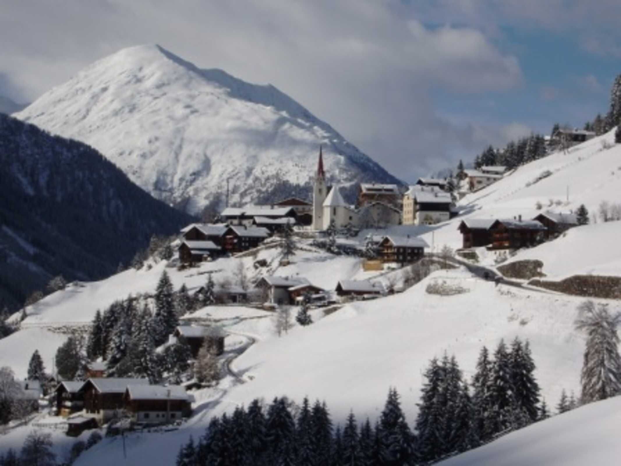 A snow-covered village with traditional wooden houses, a church, and a mountain in the background.