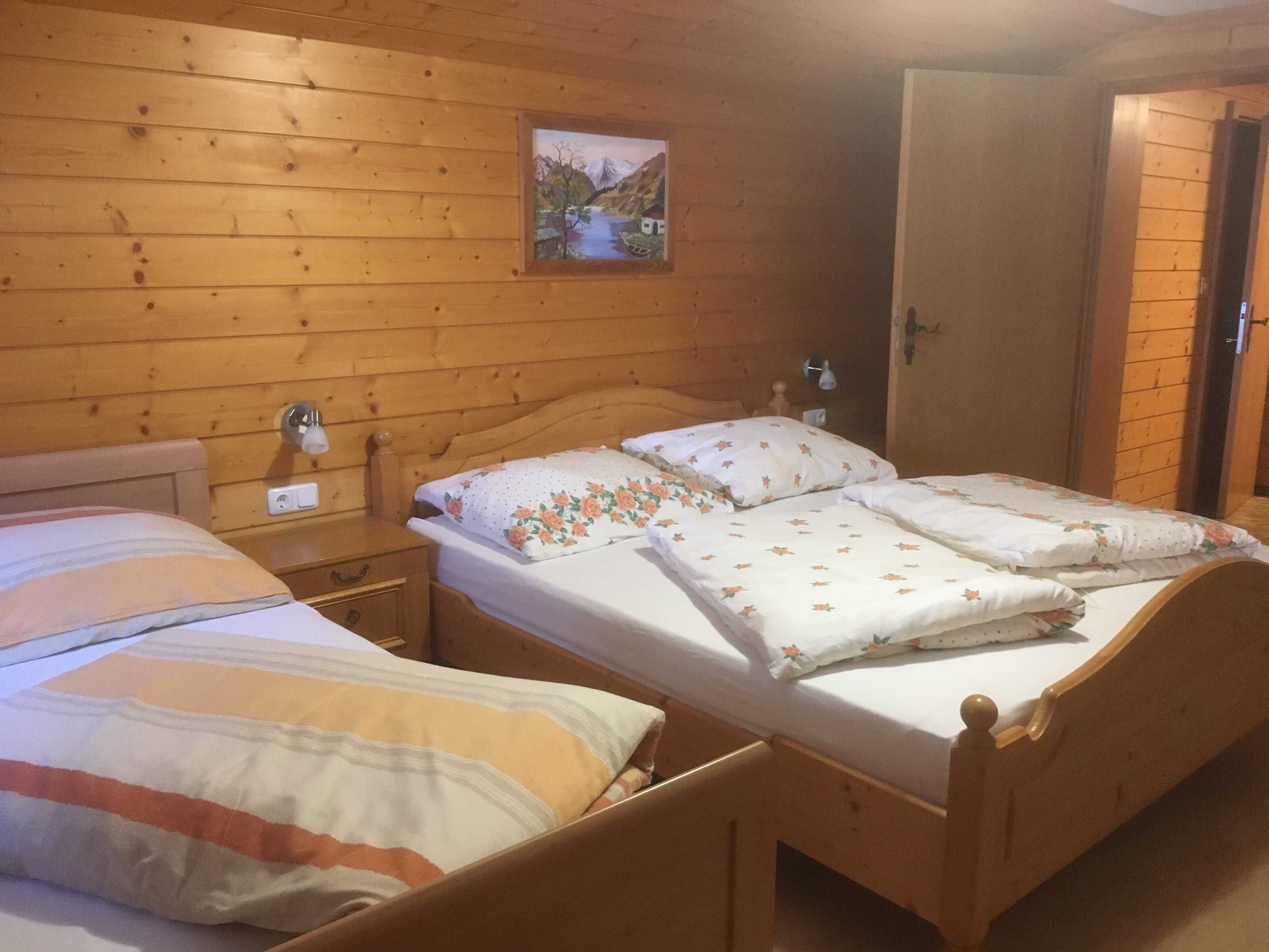 Une pièce aux murs lambrés, comprenant deux lits, une table de chevet, une lampe fixée au mur et une porte.