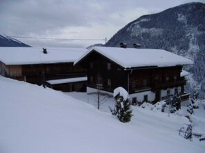 Eine Holzhütte mit schneebedecktem Dach, umgeben von schneebedeckten Bäumen und Bergen.