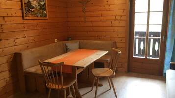 A wooden cabin with a dining table, chairs, a bench, a crucifix, and a painting on the wall.