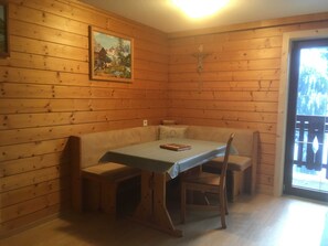 Et interiør af en træhytte med et spisebord, bænke, et maleri og et krucifiks på væggen.