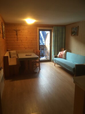 Et hyggeligt rum med træpaneler, et spisebord, en sofa og udsigt gennem en glasdør.