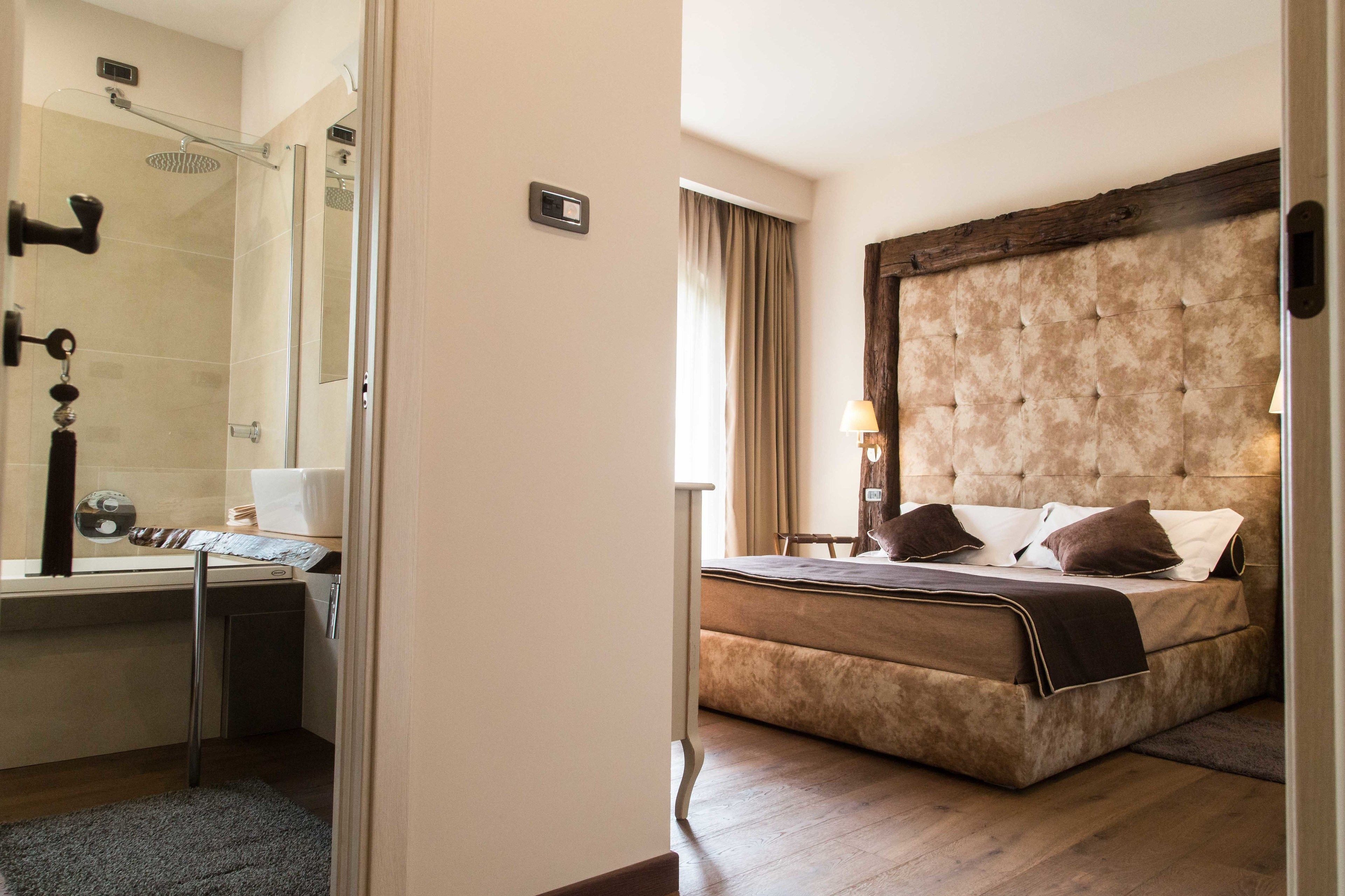 A hotel room with a shower, a bed with a tufted headboard, a bedside table, and a window with curtains.