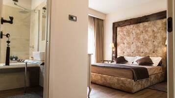A hotel room with a shower, a bed with a tufted headboard, a bedside table, and a window with curtains.