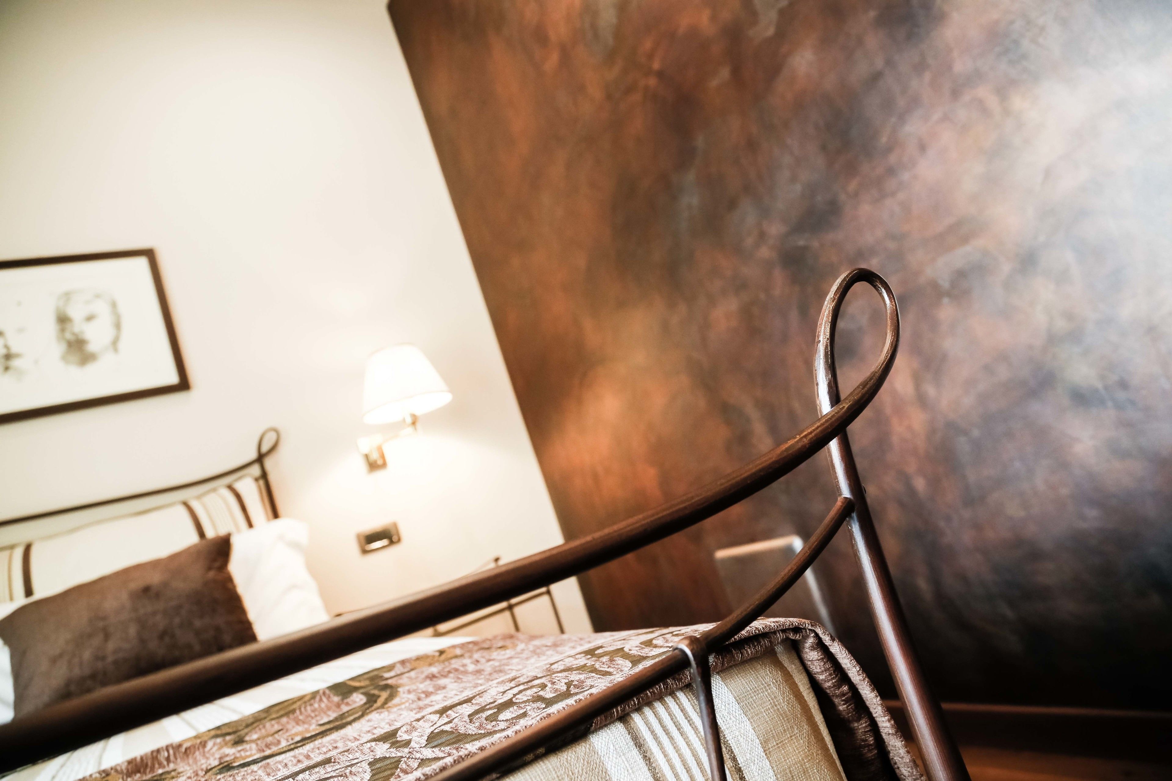 A bed with a patterned bedspread, a headboard, and a wall-mounted lamp.