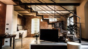 Una cocina moderna con pared de ladrillo, un comedor con mesa y sillas, y una escalera con barandilla metálica.
