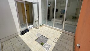 Un patio soleado con puerta corrediza de vidrio que da a un dormitorio, un pequeño jardín con plantas y un par de zapatos cerca de la puerta.