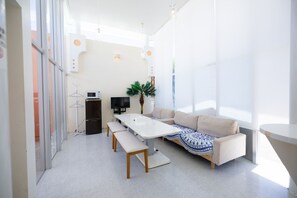 A modern, well-lit room with a white table, beige sofa, and a TV. - Nirai Beach Villa (Yomitan)