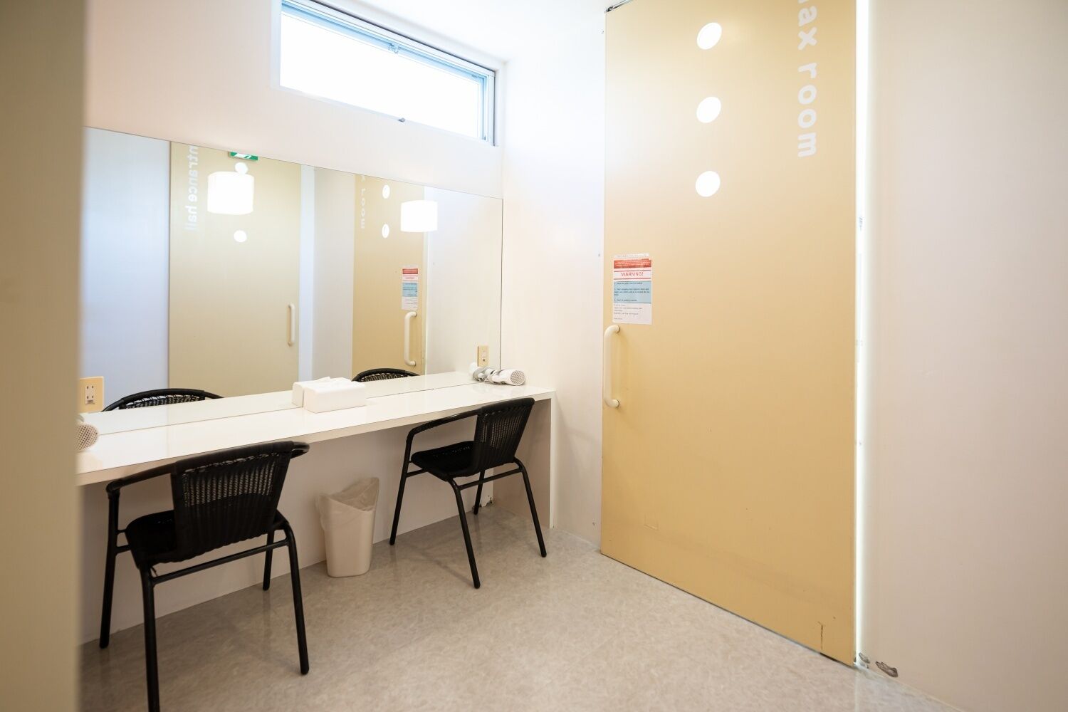 A bathroom with a white sink, two black chairs, a mirror, and a door with a warning sign.