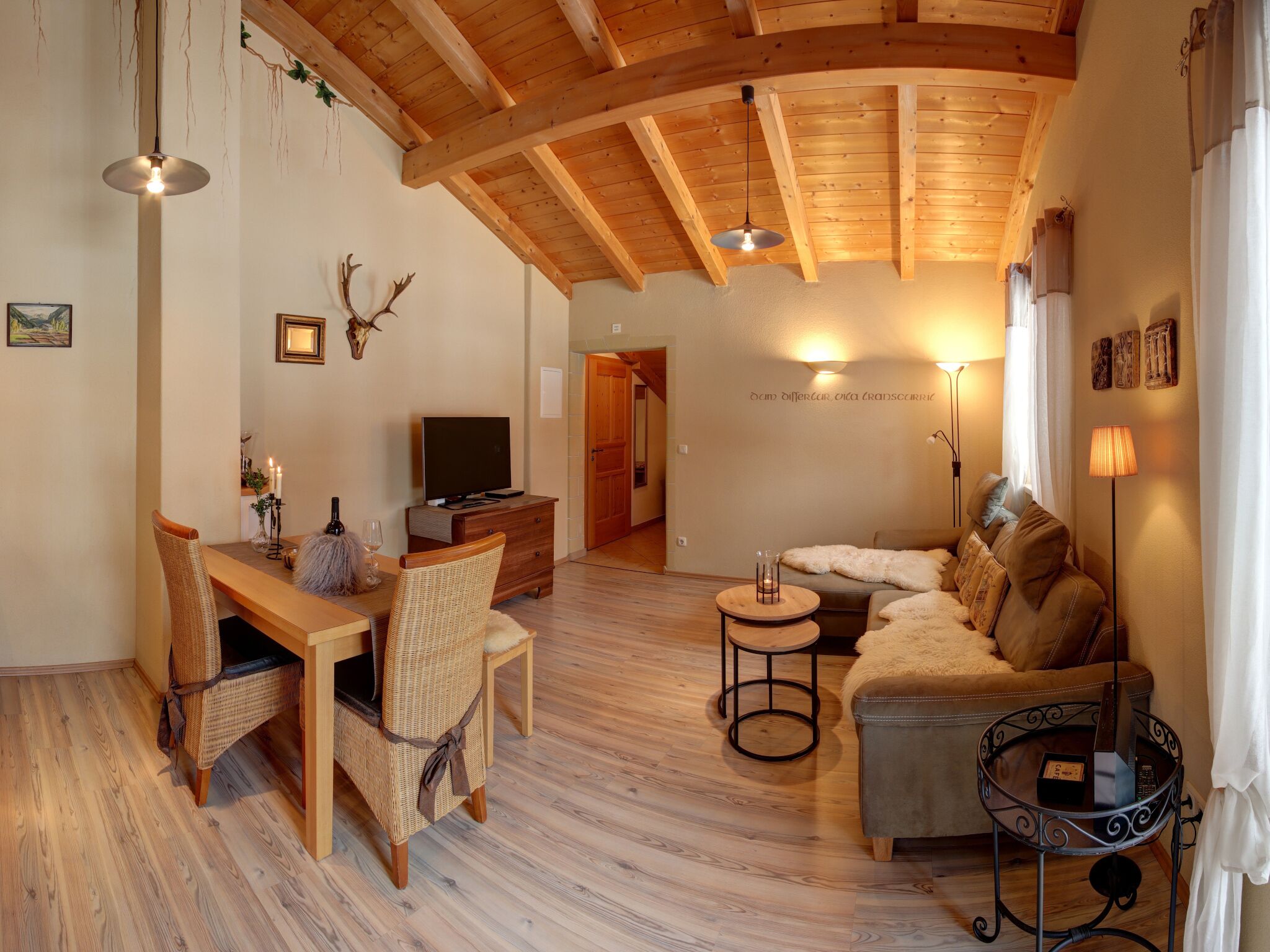 Un salon chaleureux avec un plafond en bois, un téléviseur, un coin repas avec des chaises en osier et un canapé.