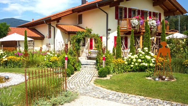 Ein traditionelles Chalet mit einem Kiesweg, der zum Eingang führt, umgeben von einem gepflegten Garten mit verschiedenen Pflanzen und Blumen.
