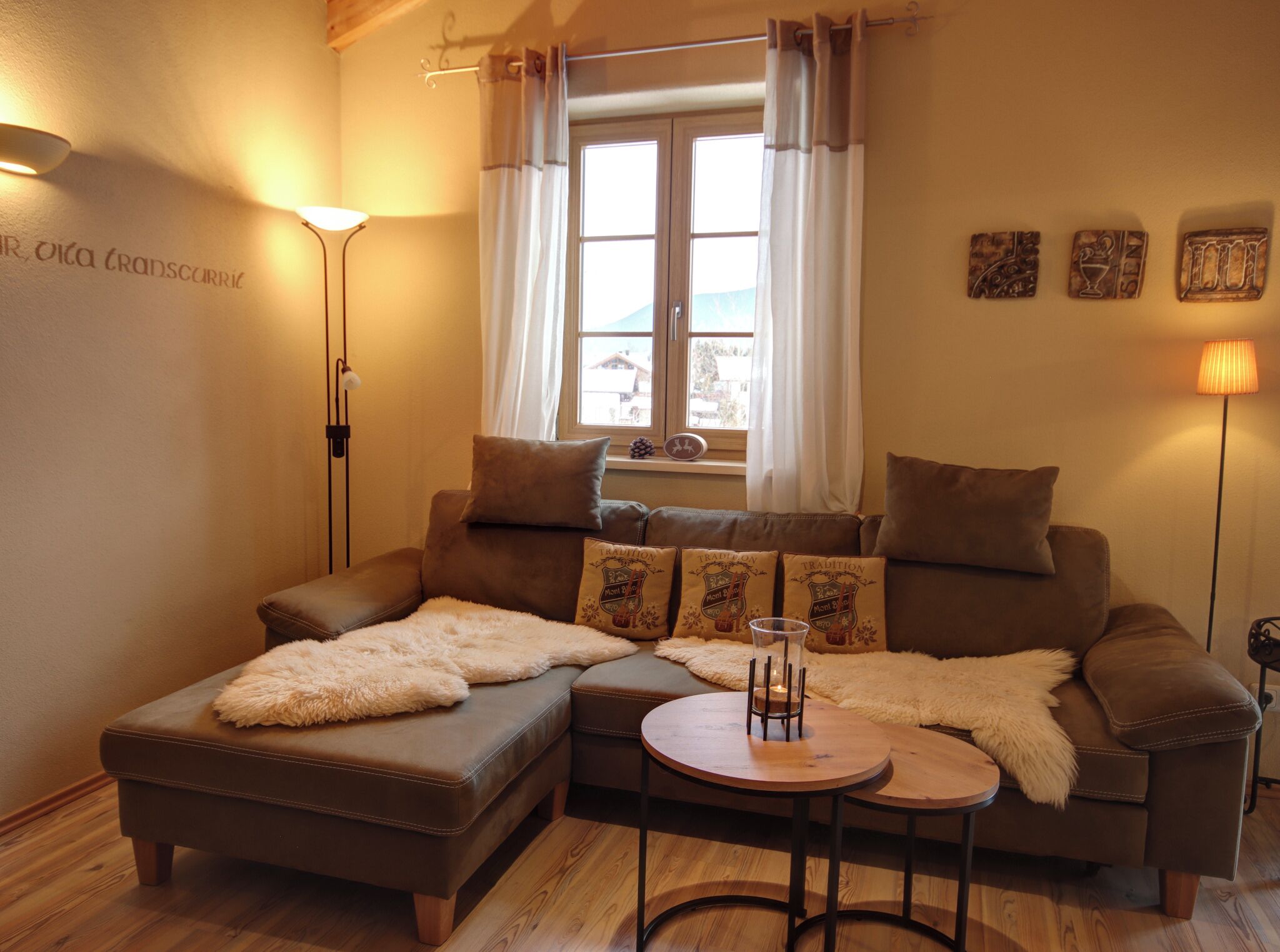 A cozy living room with a brown leather sofa, a small round table, and a window with curtains.