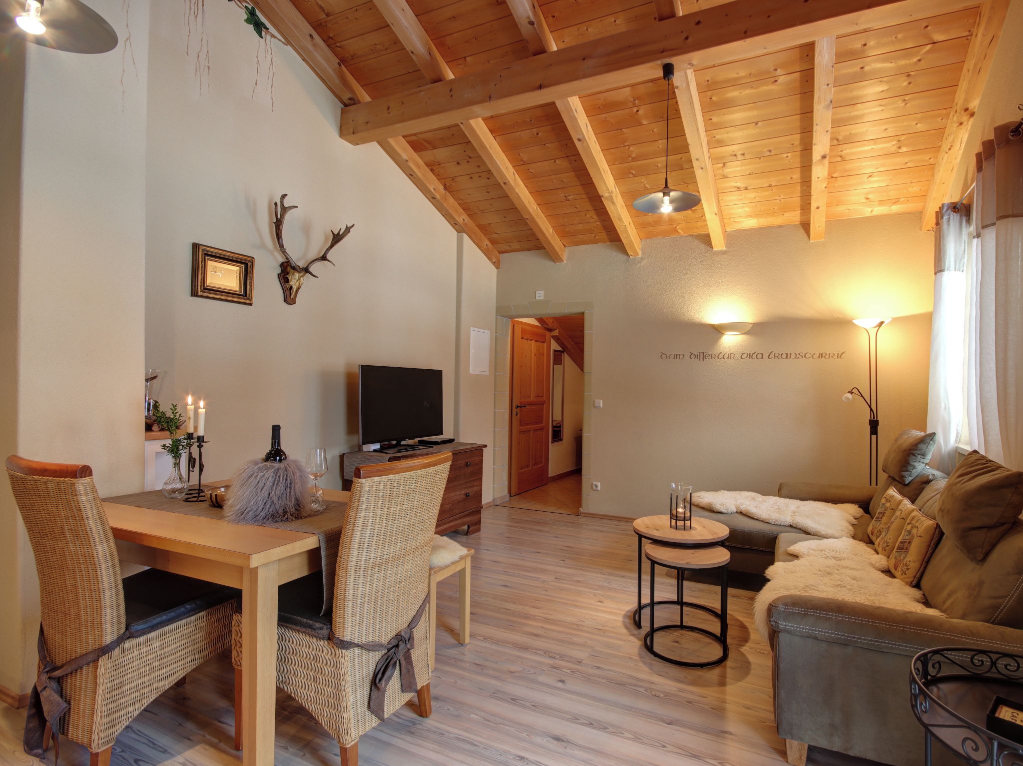 Un salon chaleureux avec un plafond en bois, un téléviseur, un canapé et un coin repas comprenant des chaises et une table en osier.