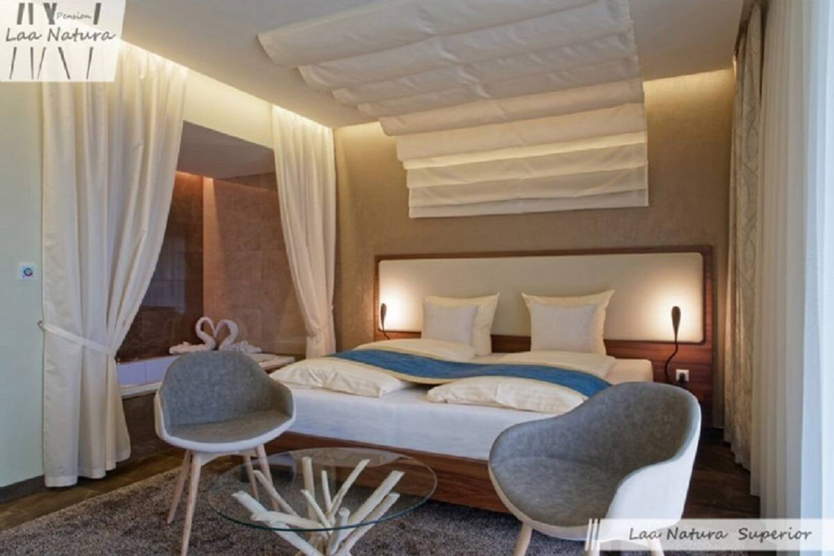 Une chambre d’hôtel moderne avec un grand lit, deux fauteuils, une table basse en verre et un luminaire au plafond.