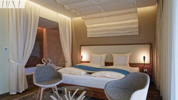 Een moderne hotelkamer met een groot bed, twee fauteuils, een glazen salontafel en een plafondlamp.