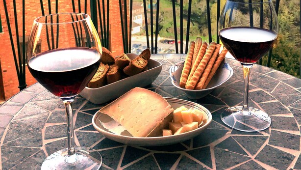 Ein Tisch mit Weingläsern, Brot und einer Schüssel mit Snacks auf einem Balkon mit Blick auf eine Stadtlandschaft und historische Gebäude.