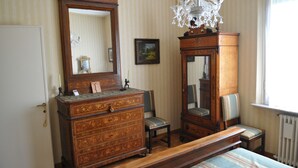 Ein Schlafzimmer mit einem Holzkasten, einem Sessel, einem Bett, einem großen Spiegel und einer Chandelieber.