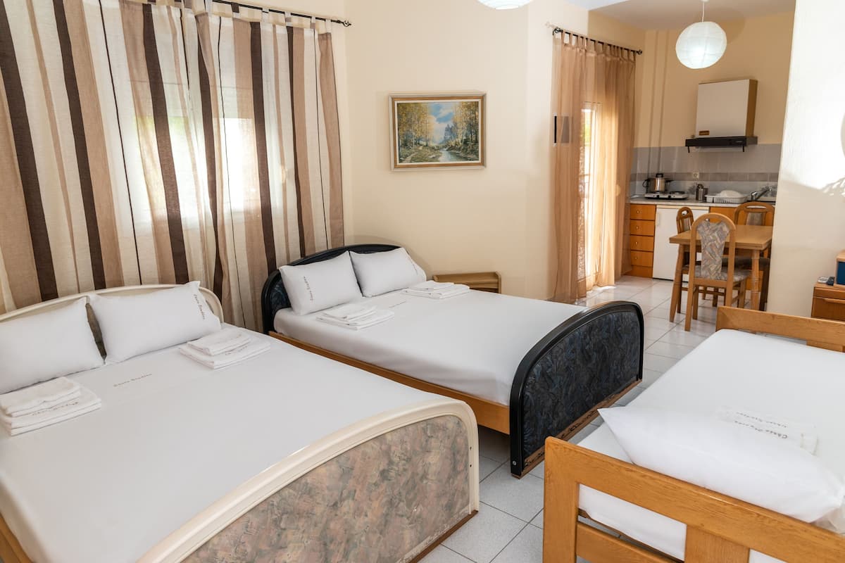 A hotel room with two single beds, a small kitchenette, a dining area, and a painting on the wall.