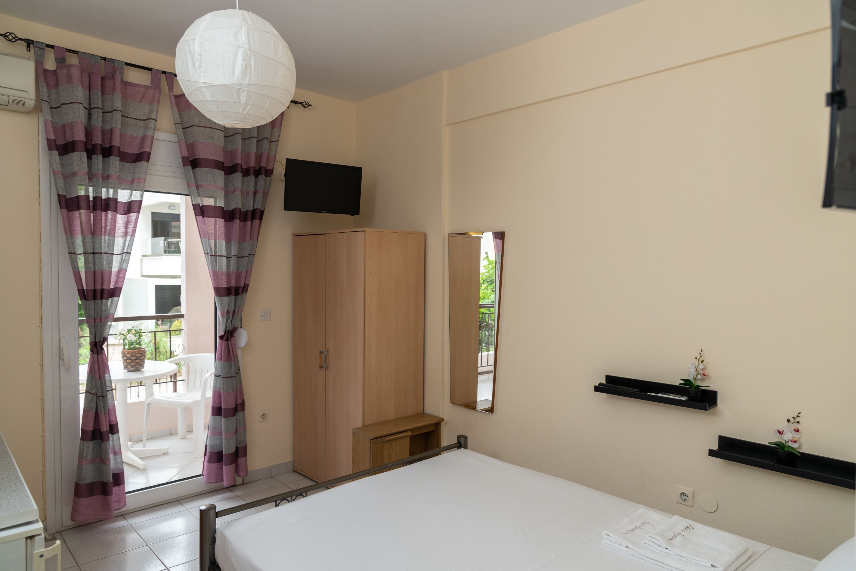 Une chambre à coucher comprenant un lit, une armoire, un téléviseur et un balcon avec des rideaux.