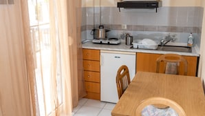A compact kitchen with a white refrigerator, a sink, and a stove. There is a wooden dining table with chairs. - Chris Apartments (Kassandra)