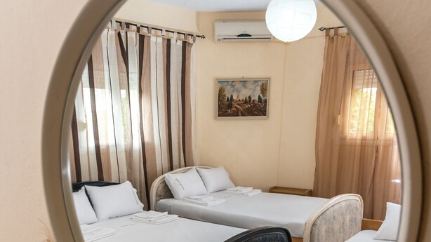 A hotel room with two beds, a round mirror, a small table, and a vase of flowers. - Chris Apartments (Kassandra)
