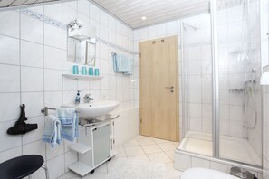 A bathroom with a sink, mirror, towel rack, shower, and a door. - Haus Sonnenhügel (Winterberg)