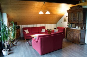 A cozy living room with a red sofa, a wooden cabinet, and a potted plant. - Haus Sonnenhügel (Winterberg)