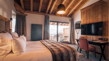 Une chambre avec un grand lit, un bureau, une télévision et un balcon offrant une vue sur les montagnes.