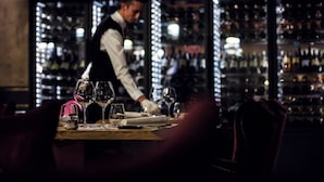 A bar setting with a bartender, a well-stocked wine rack, and a table with wine glasses and a menu. - Hôtel Daria-I Nor by Les Etincelles (Huez)