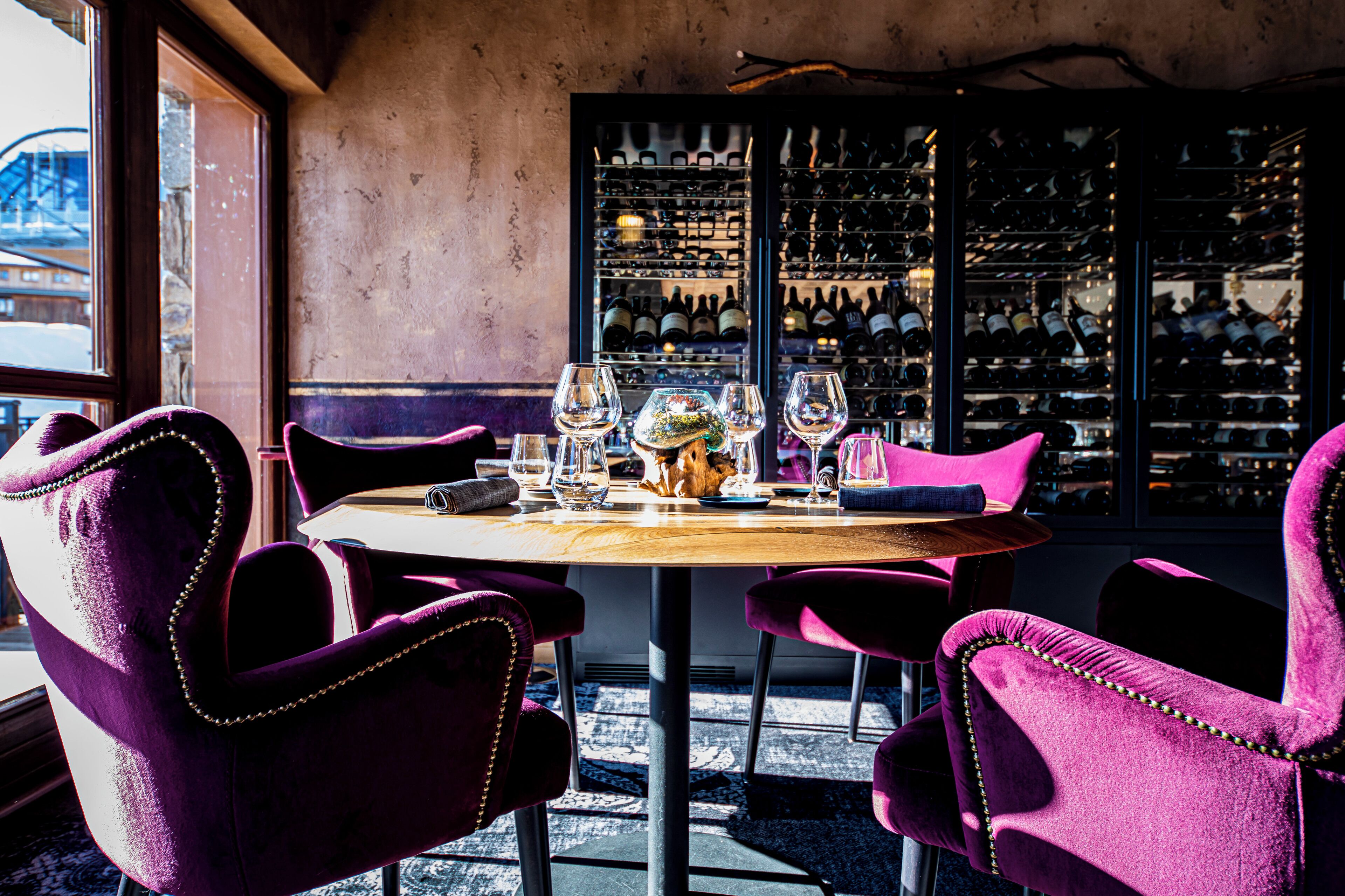 A round table with chairs, a wine rack in the background, and a view of the outside.