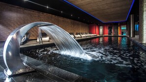 A modern indoor pool with a waterfall feature, wooden ceiling, and red accent walls. - Hôtel Daria-I Nor by Les Etincelles (Huez)