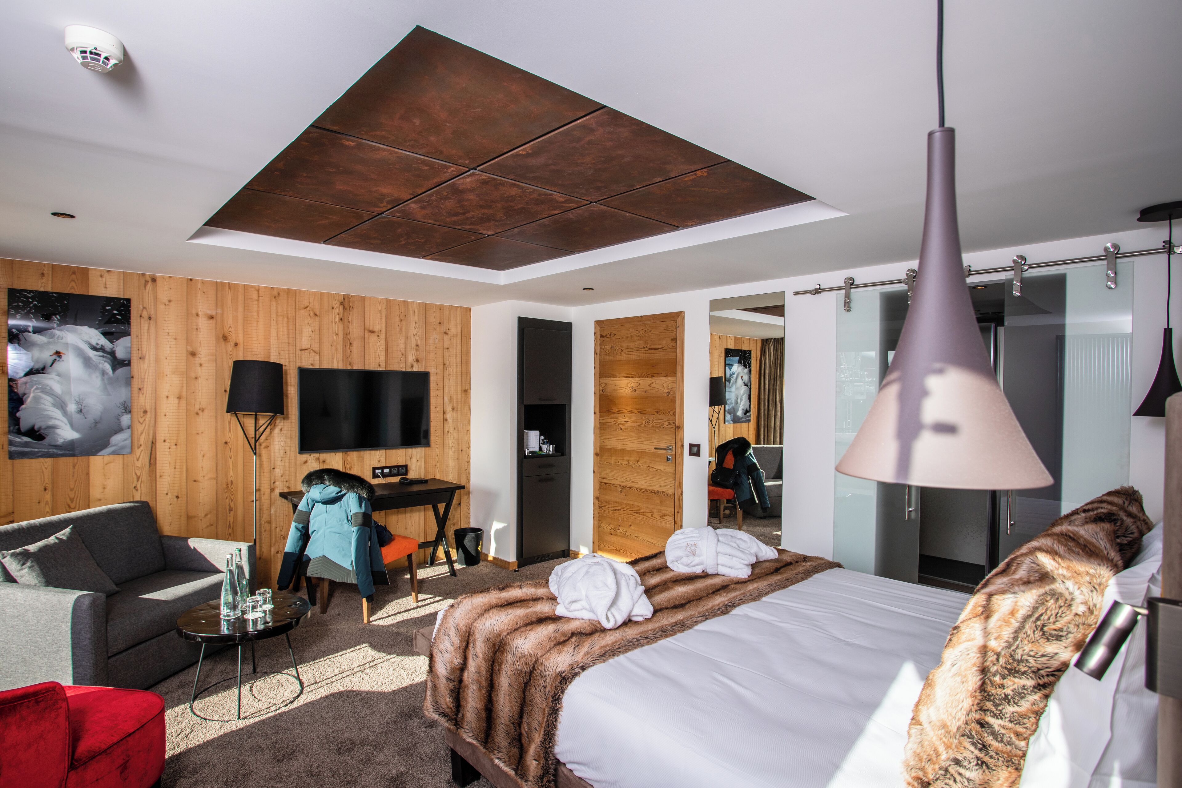 Quarto de hotel moderno com uma cama grande, um sofá, uma escrivaninha e uma televisão.