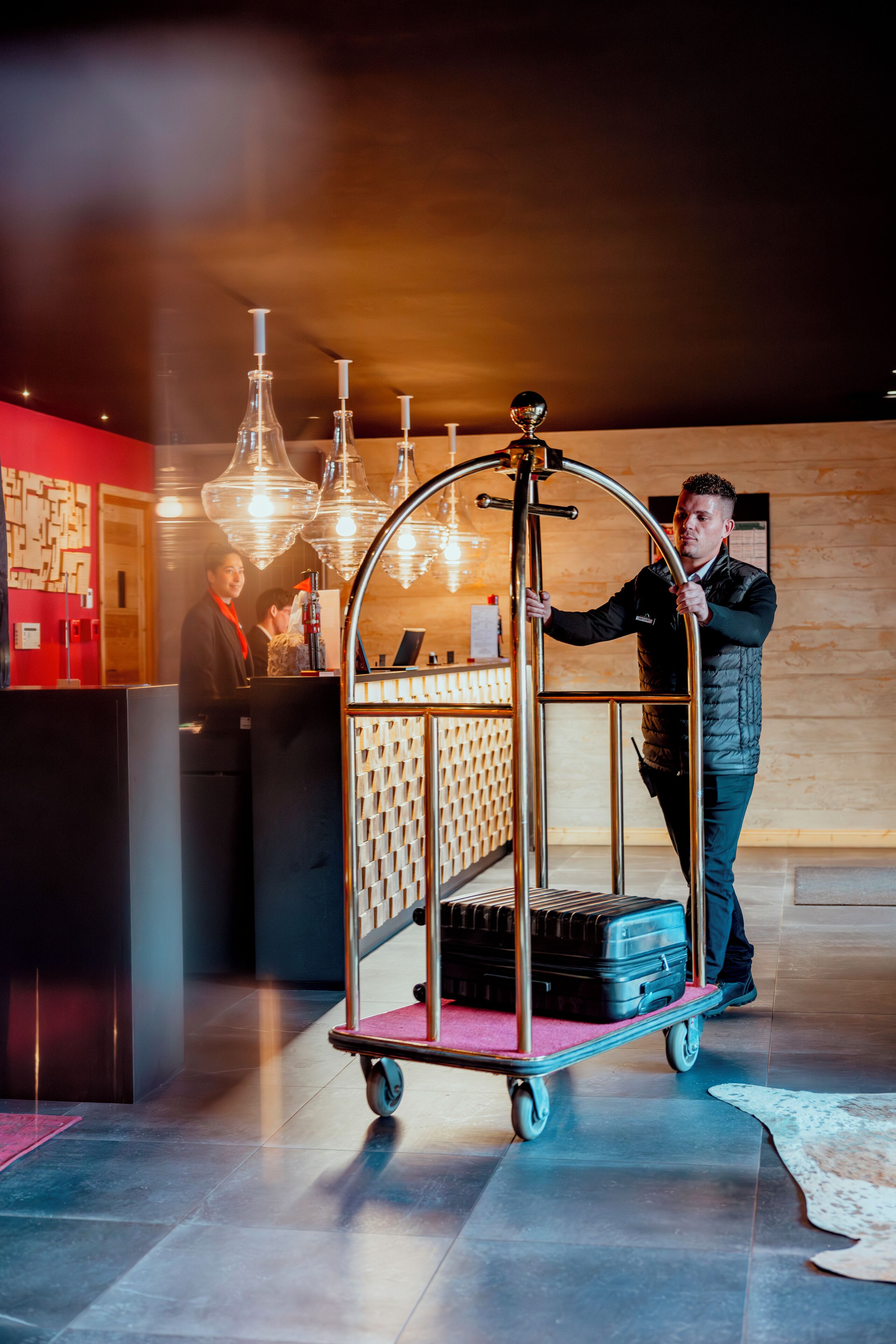Ein Hotel-Empfangsbereich mit Gepäckwagen, Empfangsschalter und einer Holzwand.