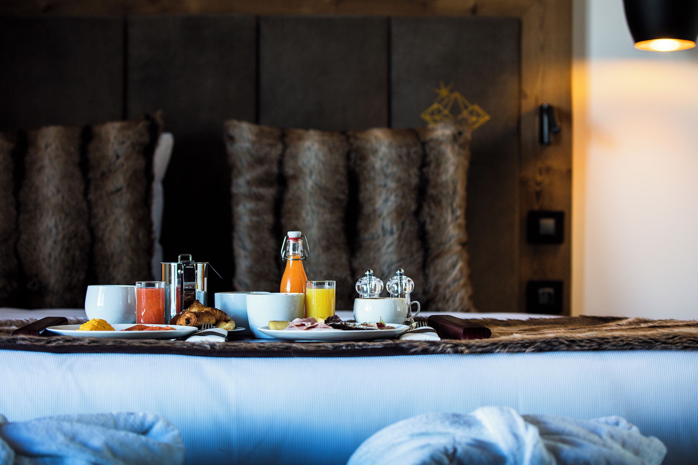 A breakfast setup on a bed with a wooden headboard, including plates, cups, and a bottle.