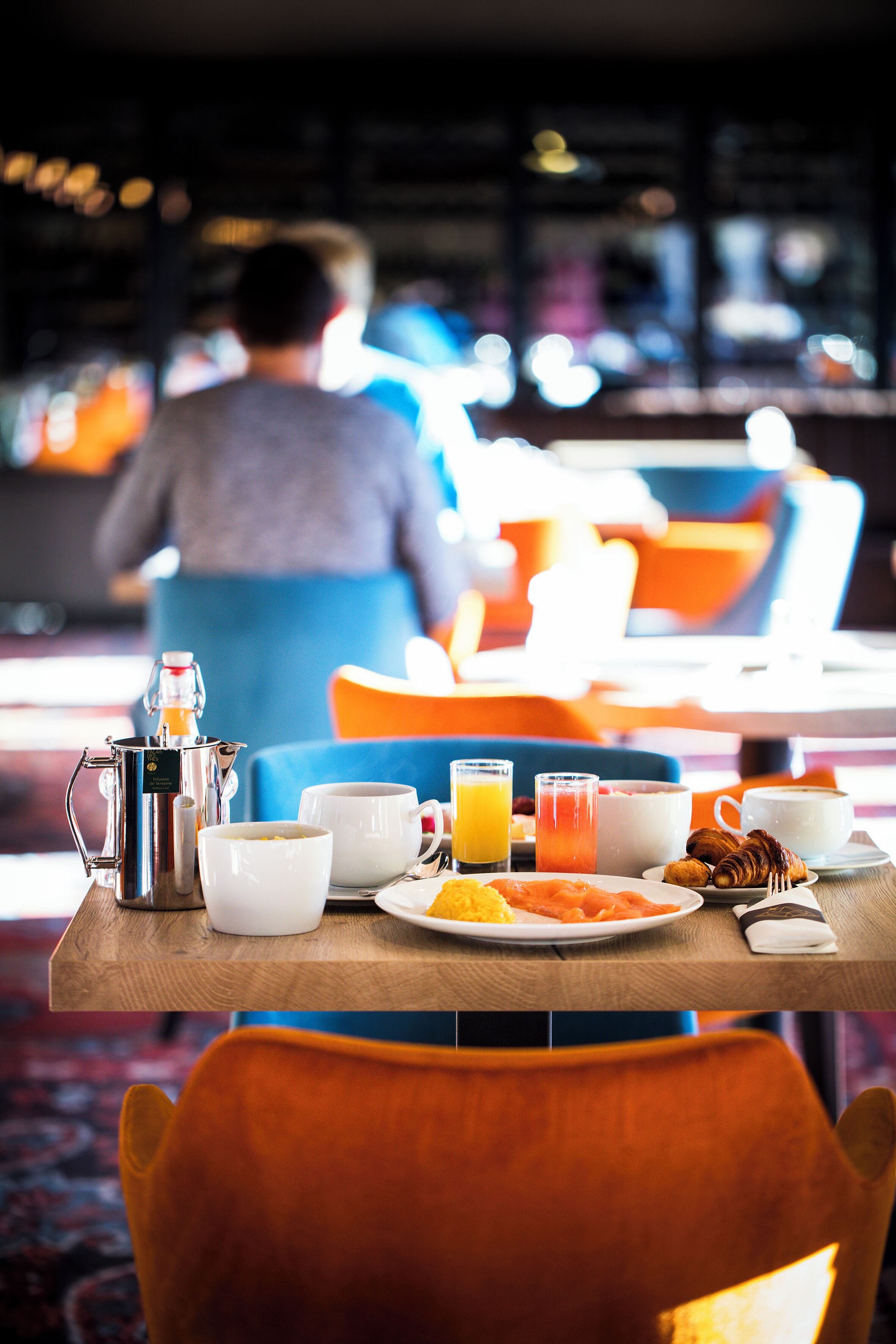 A breakfast table with coffee, juice, croissants, and a plate of food.