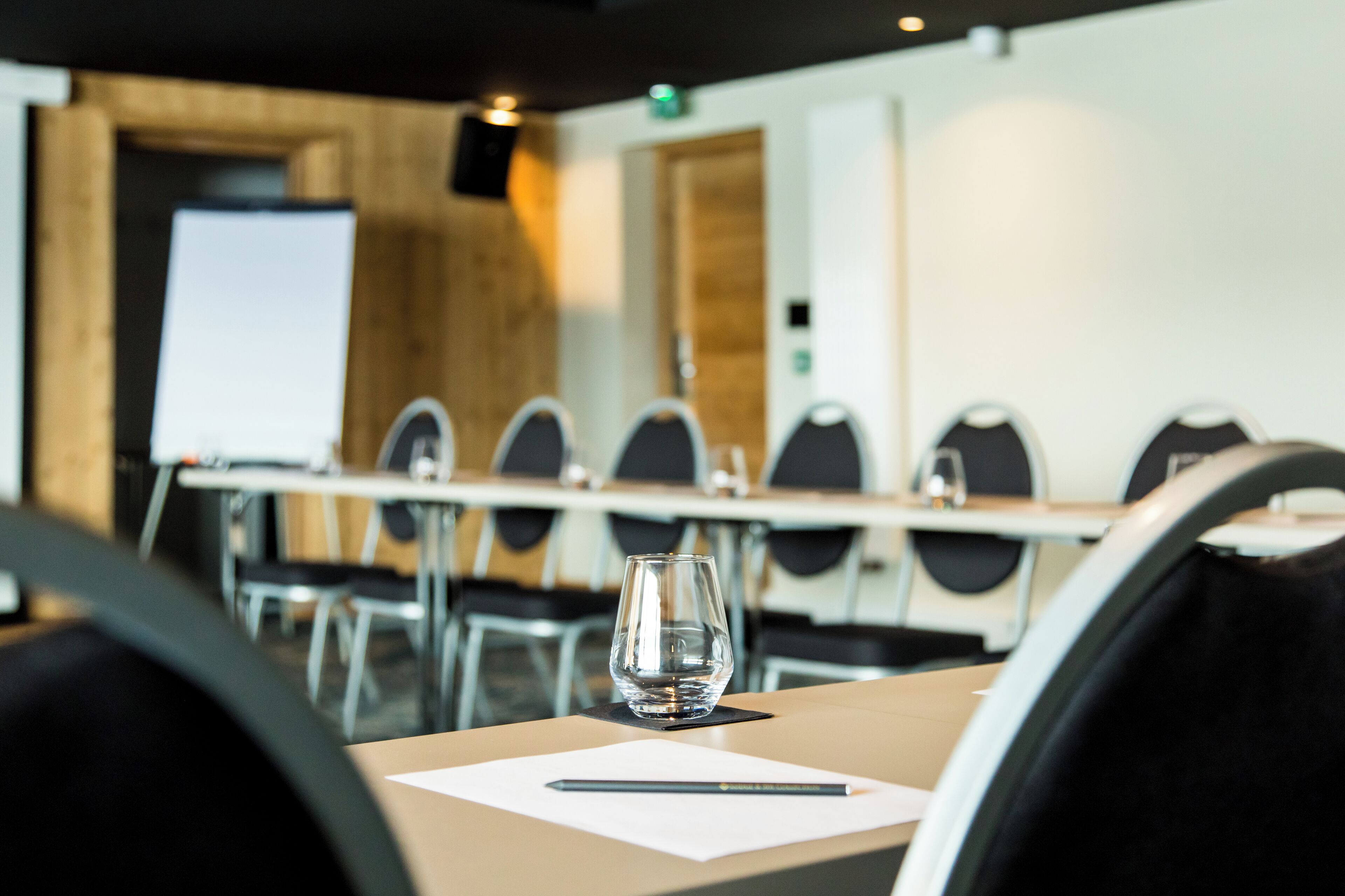 A conference room with a table, chairs, a glass of water, and a notepad.