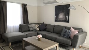 Una sala de estar moderna con un sofá seccional gris, una mesa de centro de madera y un ventanal con cortinas.