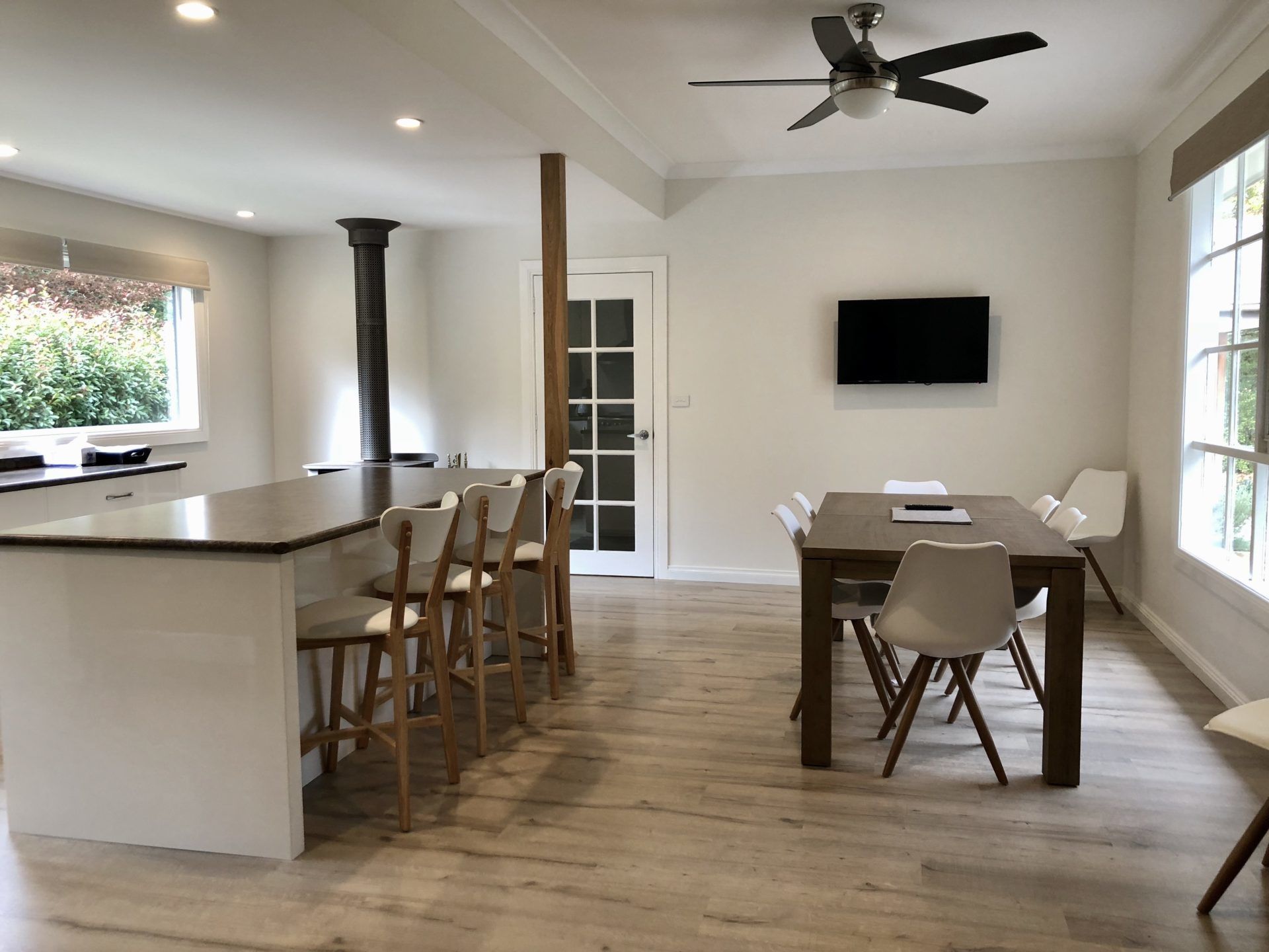 A modern kitchen with a central island, wooden chairs, a dining table, and a ceiling fan.