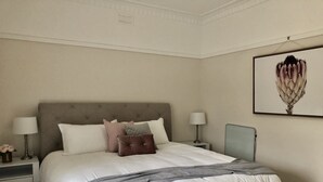Un dormitorio ordenado con una cama grande, dos mesitas de noche y una lámpara de pared.