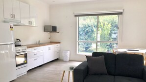 Una cocina moderna con armarios blancos, horno empotrado y microondas. Se ve una ventana con vistas a la vegetación.